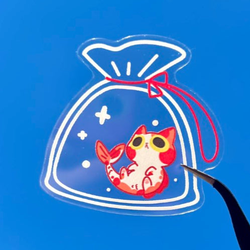 Hand holding a small bag with a cartoon character against a clear blue sky.